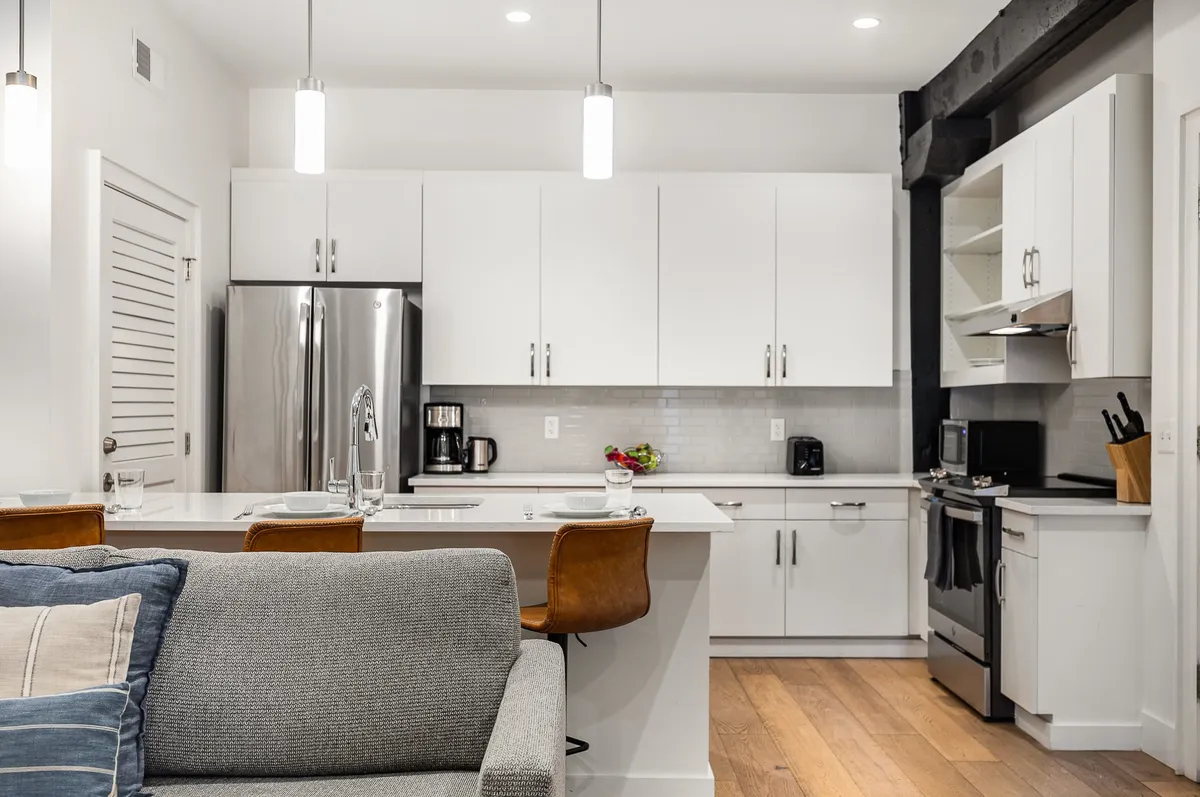 A wide-angle view reveals a bright kitchen anchored by a large island with bar stools. Stainless steel appliances and decorative touches make the space feel ready for entertaining, while soft lighting highlights the inviting, functional layout.