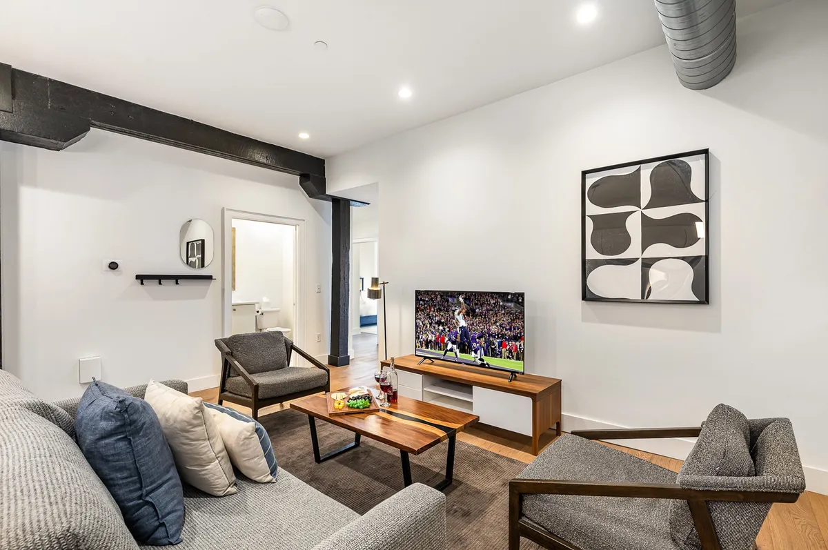 A cozy living room scene with a TV displaying a sports event, a coffee table set with drinks, and decorative wall art. The casual arrangement suggests a space perfect for relaxing, socializing, or enjoying a movie or game night with friends.