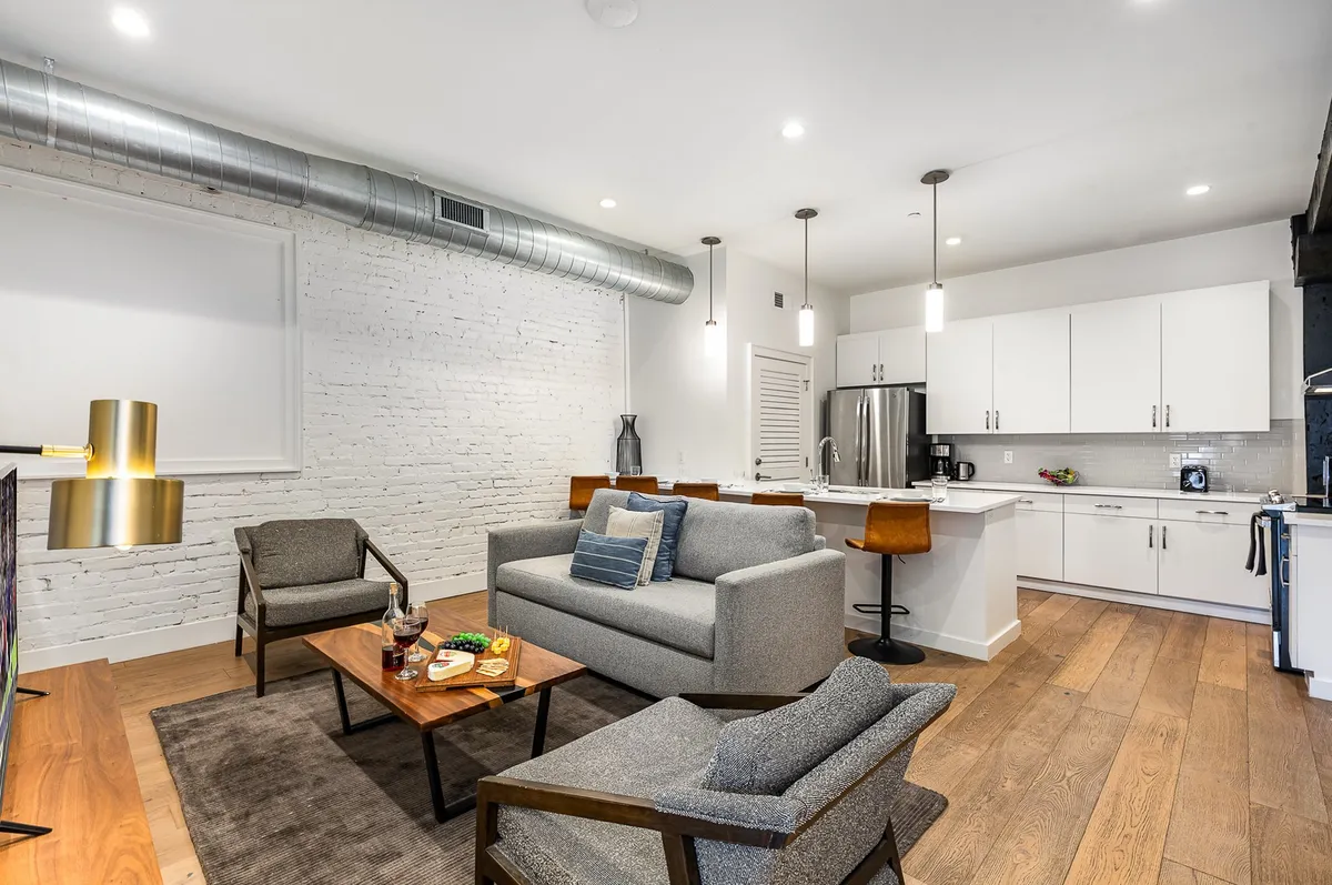 A comfortable and stylish living area featuring a plush sofa, a coffee table, an adjacent kitchen space, and modern lighting fixtures. The layout encourages relaxation and easy conversation among guests.