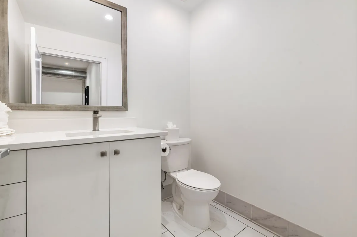 A minimalist, serene half bathroom with a vanity sink, large mirror, and toilet. The design highlights modern fixtures and a calm, uncluttered atmosphere, ideal for quick refreshes between outings.