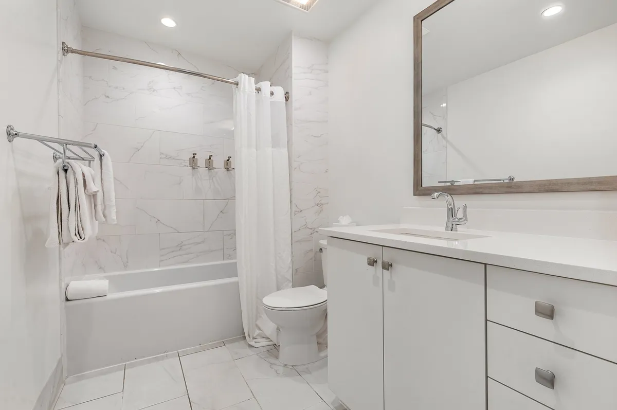 A tranquil and inviting bathroom featuring a bathtub with a shower curtain, a sleek vanity, and a large mirror. Clean lines, fresh towels, and modern fixtures create a serene atmosphere ideal for relaxation or a quick refresh. Starter toiletries are subtly visible, reinforcing guest convenience.