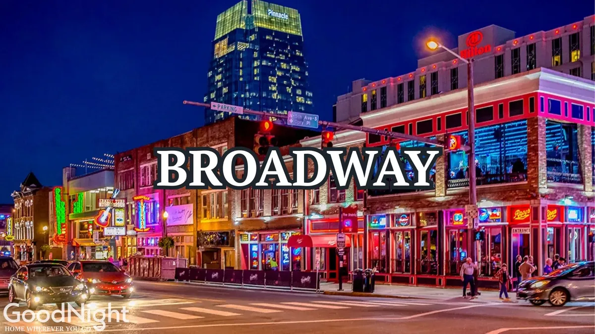This exterior image captures the heart of downtown Nashville nightlife with colorful storefronts, glowing neon lights, a bustling street, and people walking. The energy and vibrancy are palpable, reflecting the iconic honky-tonks and late-night adventures just steps from the Saddlery building.